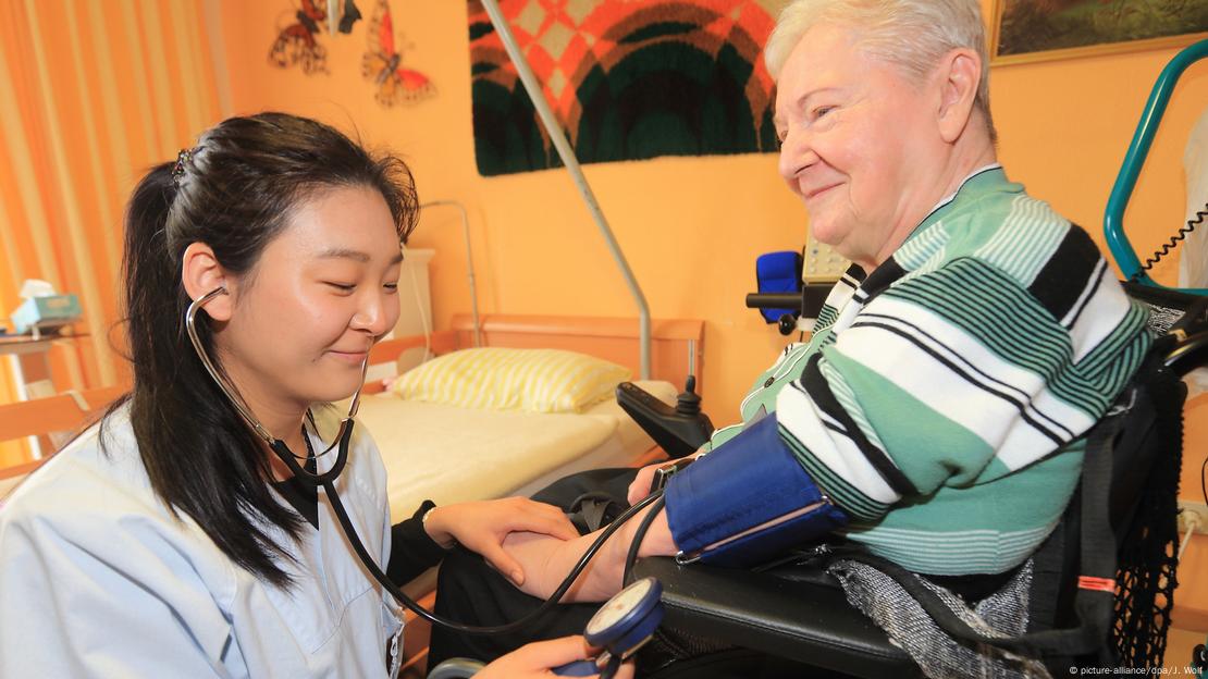 Chinese nurse tending to old German woman in nursing home