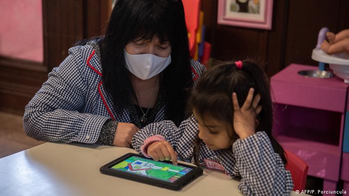 Una maestra con barbijo enseña con una tablet a una niña en el jardín de infantes en Uruguay.