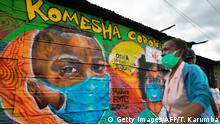 A woman wearing a face mask walks past a mural advocating safety practices to curb the spread of the novel coronavirus (Covid-19) at Mathare slum April 29, 2020 in the Kenyan capital, Nairobi. (Photo by TONY KARUMBA / AFP) (Photo by TONY KARUMBA/AFP via Getty Images)