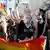 Jovens com máscara levantam o punho segurando bandeira arco-íris