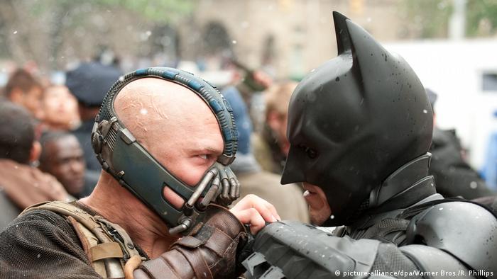 Bane, wearing a mask over his mouth, fights fist to fist with Batman.