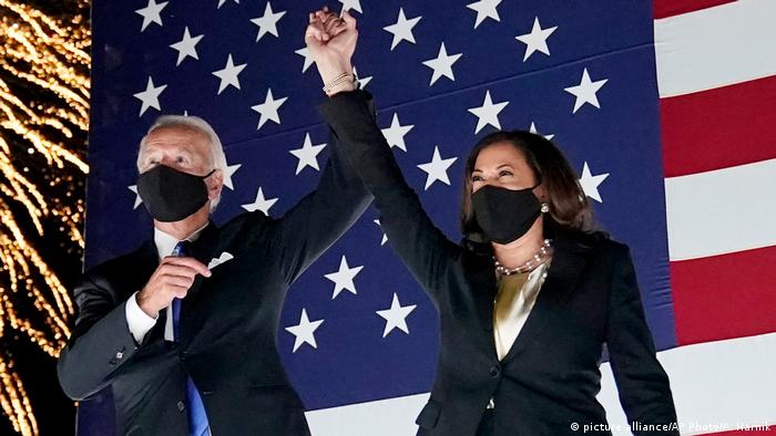 Joe Biden and Kamala Harris raise their hands against the American flag at the Democratic National Convention