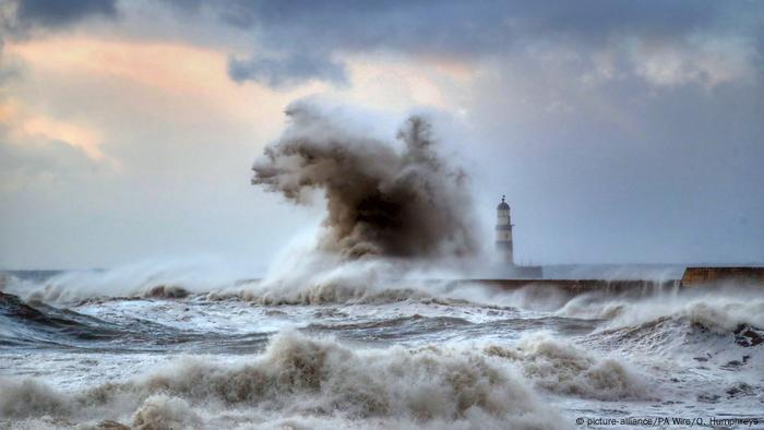 Vast waves crash against a lighthouse