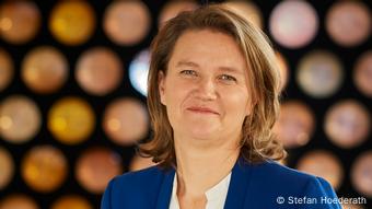 Andrea Zietzschmann mit knallblauem Sakko, im Hintergrund ist eine verschwommene Wand mit Kreisen zu sehen (Foto: Stefan Hoederath).