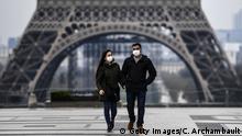 A couple wearing protective mask walks by the Esplanade du Trocadero square near the Eiffel Tower in Paris, on March 18, 2020, a day after a strict lockdown came into effect in France to stop the spread of the COVID-19, caused by the novel coronavirus. - A strict lockdown requiring most people in France to remain at home came into effect at midday on March 17, 2020, prohibiting all but essential outings in a bid to curb the coronavirus spread. The government has said tens of thousands of police will be patrolling streets and issuing fines of 135 euros ($150) for people without a written declaration justifying their reasons for being out. (Photo by Christophe ARCHAMBAULT / AFP) (Photo by CHRISTOPHE ARCHAMBAULT/AFP via Getty Images)