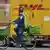 A postman of the Pin AG mail delivery company cycles past a delivery truck of DHL on May 15, 2019 in Berlin.