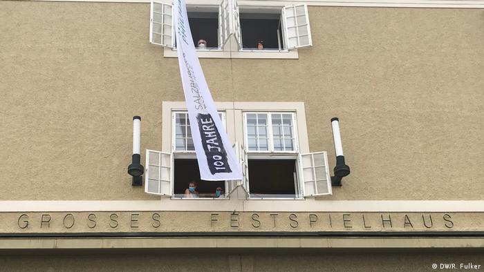 Masked visitorsr peer out of windows in the Festspielhaus