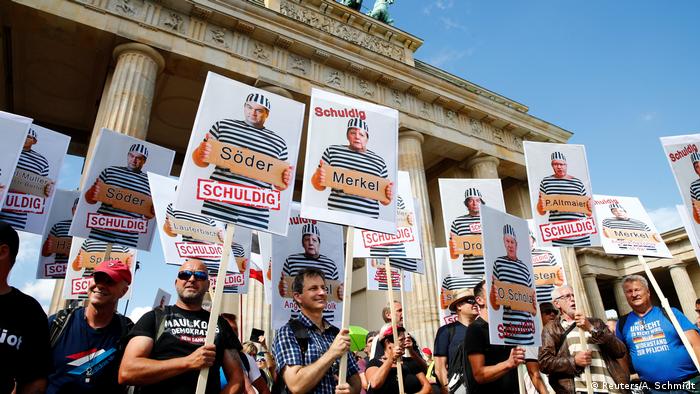 Protesters hold signs of German leaders reading 'guilty'