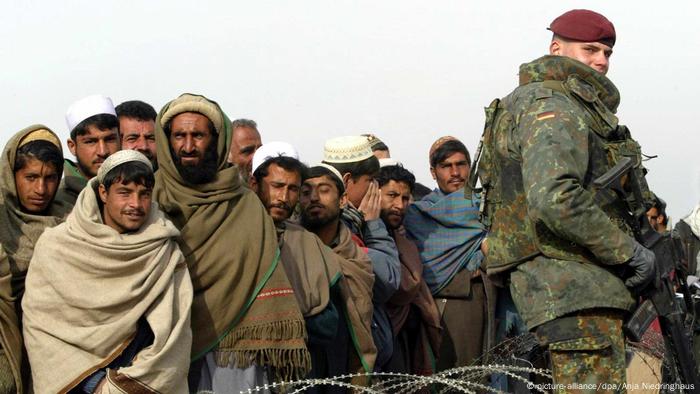 A German soldier securing a base standing in front of a group of Afghans