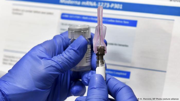 Медицинский работник в защитных перчатках держит ампулу с вакциной от коронавируса, разработанной американской компанией Moderna, и шприц