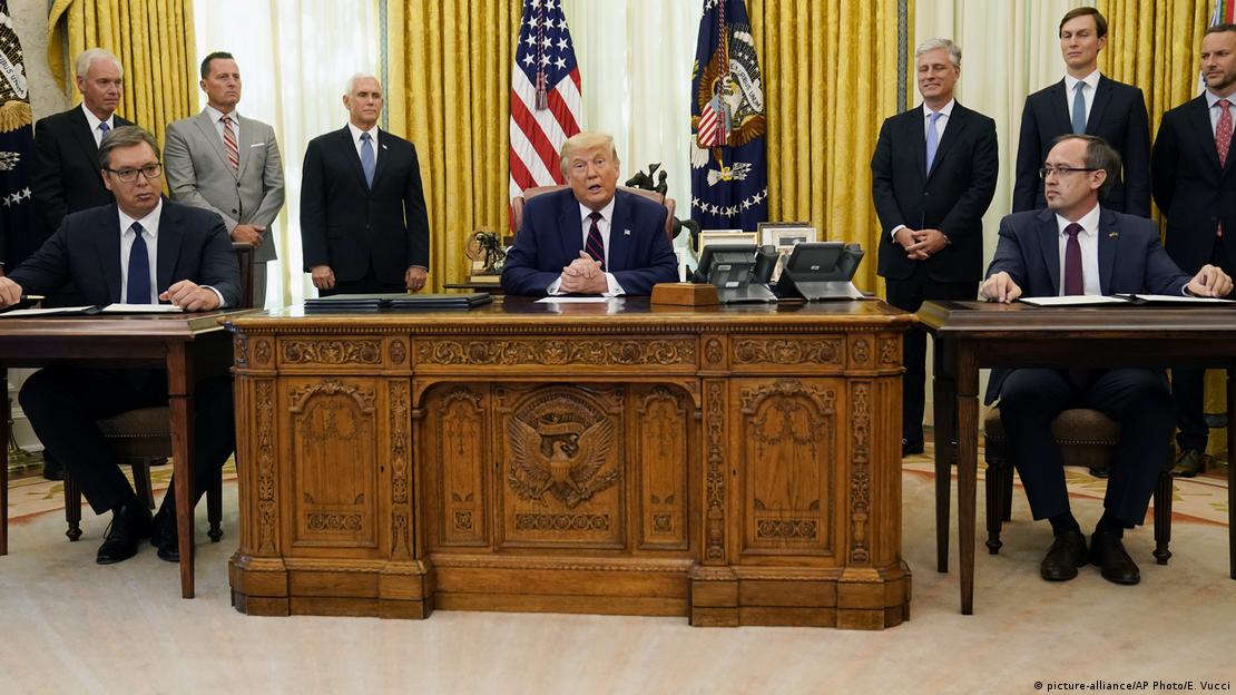 Na slici se vidi Ovalni ured Bijele kuće. U sredini, za rezbarenim stolom, sjedi Donald Trump, dok su s njegove lijeve strane Aleksandar Vučić, predsjednik Srbije, i s desne strane Avdulah Hoti, premijer Kosova. Iza njih stoje američki zvaničnici, uključujući potpredsjednika Mikea Pencea. 