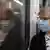 Mulher de máscara protetora, sentada em metrô, observa o próprio reflexo na janela