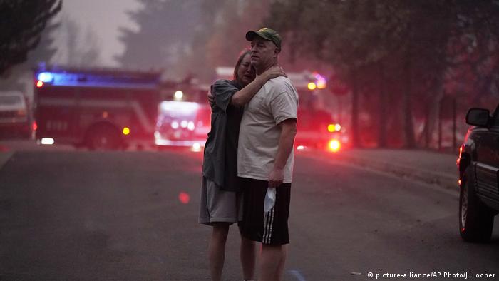 Ein Paar steht auf einer Straße mit Feuerwehrfahrzeugen und umarmt sich