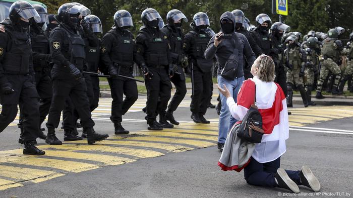 A woman with a white-red-white flank on her hips is kneeling in front of a chain of security forces