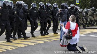 Протестующая женщина в Минске на коленях перед шеренгой силовиков