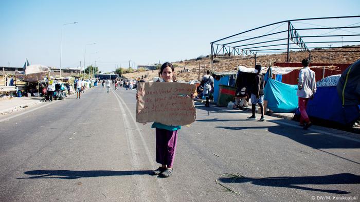 A little girl is holding a cardboard banner (in English and Dari) following the end of the protest at the makeshift tent site in front of Kara Tepe, following the Moria fire (DW/M. Karakoulaki)