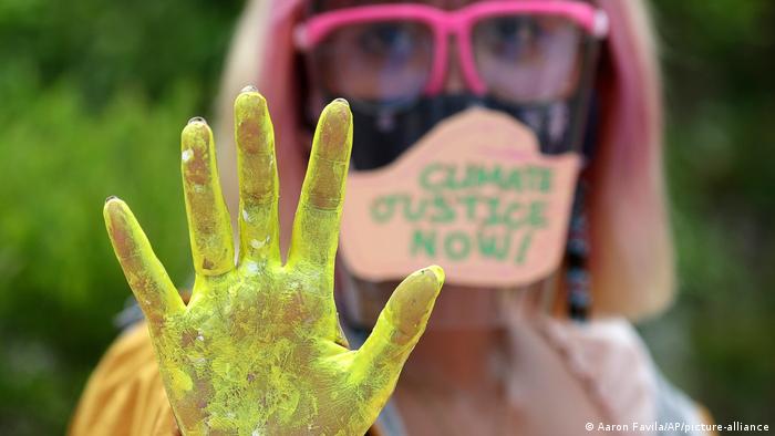 A climate protester wearing a mask holds up a yellow hand