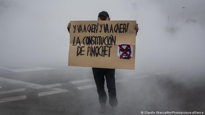 Hombre con cartel que dice: Y va a caer! Y va a caer! La Constitución de Pinochet.