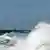 Bugwelle eines Schiffes in der Nordsee, im Hintergrund ein Windrad im Meer (Foto: ap)