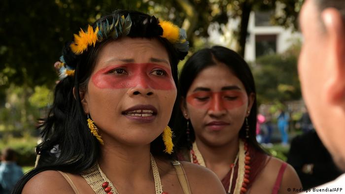 Eine Frau mit traditioneller Gesichtsbemalung und einem Kranz im Haar, die Anführerin des indigenen Volkes der Waorani, während einer Demonstration in Ecuador. Hinter ihr eine weitere Waorani 