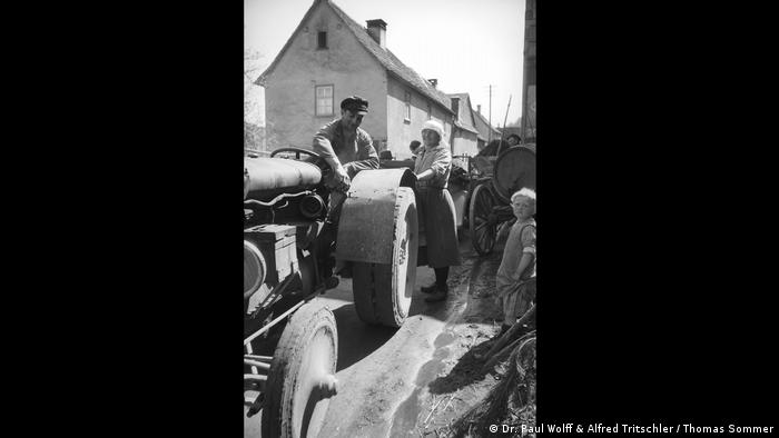 Bauer auf einem Traktor umringt von ein paar Menschen (Dr. Paul Wolff & Alfred Tritschler / Thomas Sommer)