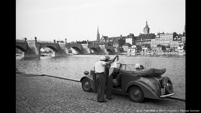 Zwei Männer vor einem parkenden Auto, das nahe der Alten Mainbrücke am Mainufer in Würzburg steht (Dr. Paul Wolff & Alfred Tritschler / Thomas Sommer)