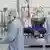 Três pessoas com roupa de proteção, máscara e touca trabalham em um laboratório. 
