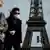 Casal de máscara anda nas ruas de Paris, com a Torre Eiffel ao fundo