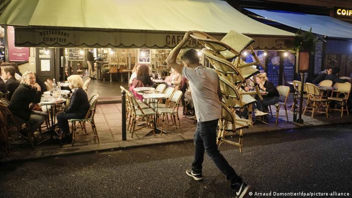 Сотрудник одного из парижских кафе убирает стулья с улицы перед закрытием