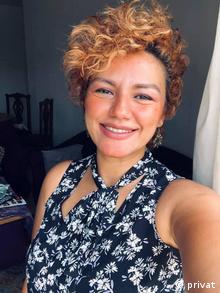 A smiling woman with light curly hair takes a selfie