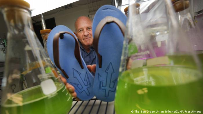 A man holds up plastic flip flops with algae to the camera. 