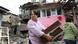 A woman carries belongings as she walks past a house damaged by recent shelling A woman carries belongings as she walks past a house damaged by recent shelling