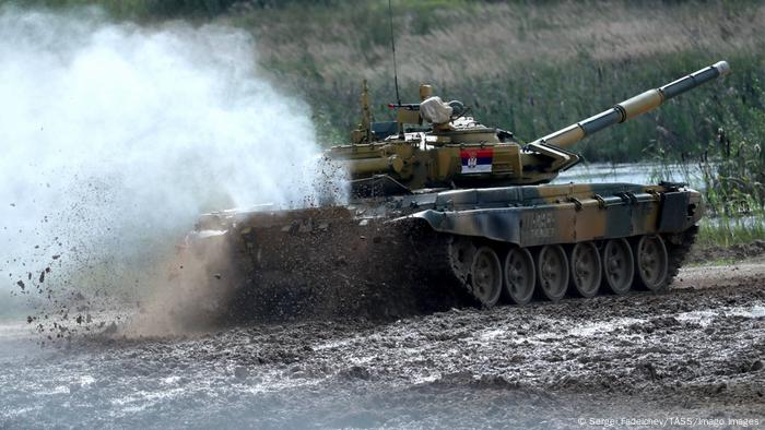 A tank drives through the mud, kicking it up in back