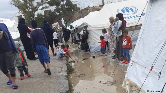 Residents of the Kara Tepe camp standing and walking near water left by heavy rainfall