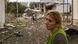 A woman stands in front of a destroyed house A woman stands in front of a destroyed house