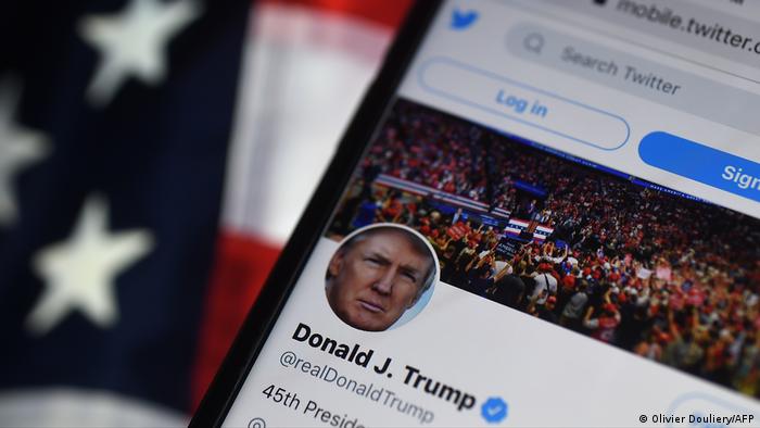 Foto simbólica de un celular con la cuenta de Donald Trump en Twitter en la pantalla y una bandera estadounidense de fondo.