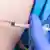 Mão com luva azul aplica vacina em uma pessoa
