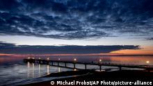 Lamps shine on a pier during sunrise at the Baltic Sea in Scharbeutz, northern Germany, Tuesday, Oct. 13, 2020. (AP Photo/Michael Probst)
