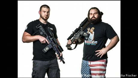 Zwei Männer halten Waffen in den Händen, einer von ihnen trägt eine Hose mit dem Muster der US-Flagge - Porträtfoto aus dem Band Divided We Stand (Mathias Braschler & Monika Fischer)
