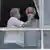 Homem e mulher idosos de máscara protetora olham para fora de janela vidraçada