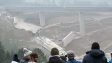 照片中几个人向山谷俯视，山谷里横亘着被炸毁的部分山谷桥