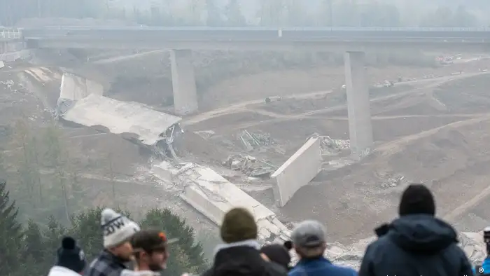 照片中幾個人向山穀俯視，山穀裏橫亙著被炸毀的部分山穀橋