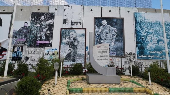 Pictures of men in military fatigues hang from a concrete wall before a stone memorial