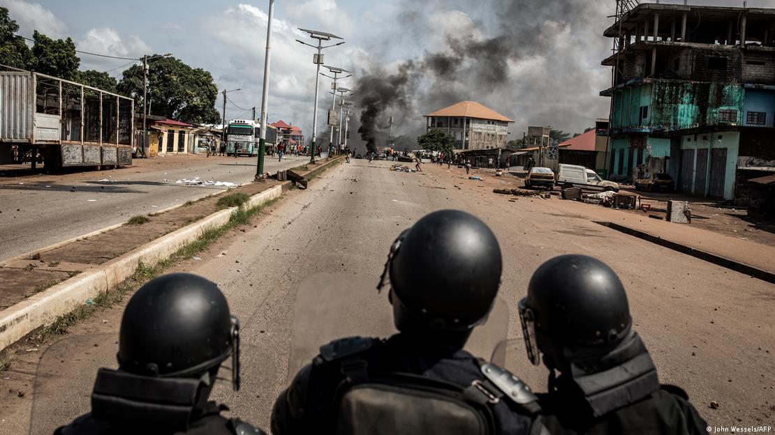 Des policiers en tenue anti-émeutes dans une rue de Conakry. On distingue de la fumée au loin.