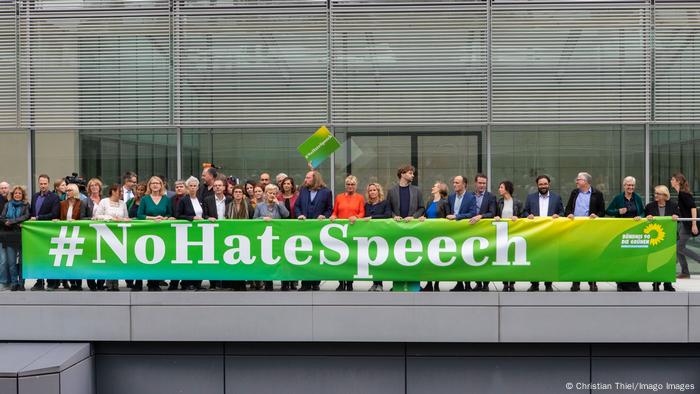 Männer und Frauen stehen hinter einem grünen Banner, auf dem steht #NoHateSpeech (ChristAan Thiel/Imago Images)