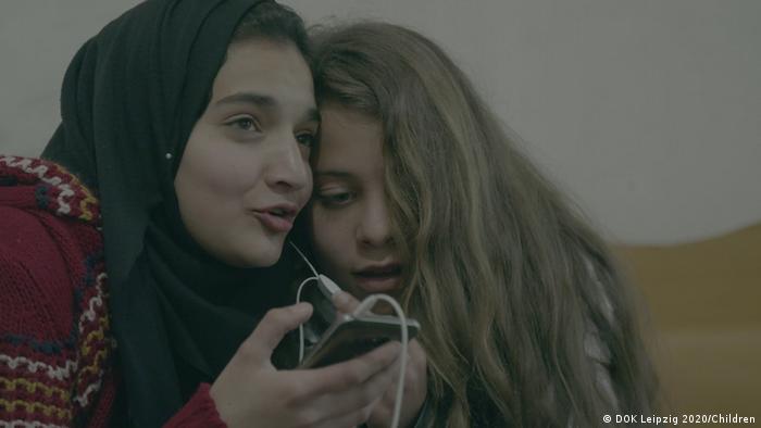 Two girls sharing earphone on a smartphone (photo: DOK Leipzig 2020/Children).