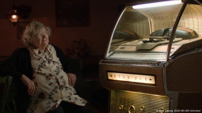 An older woman sitting next to a music vending machine. 