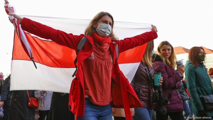 Mulher carrega em protesto bandeira que foi a de Belarus desde a independência da URSS, em 1991, até o ano de 1995