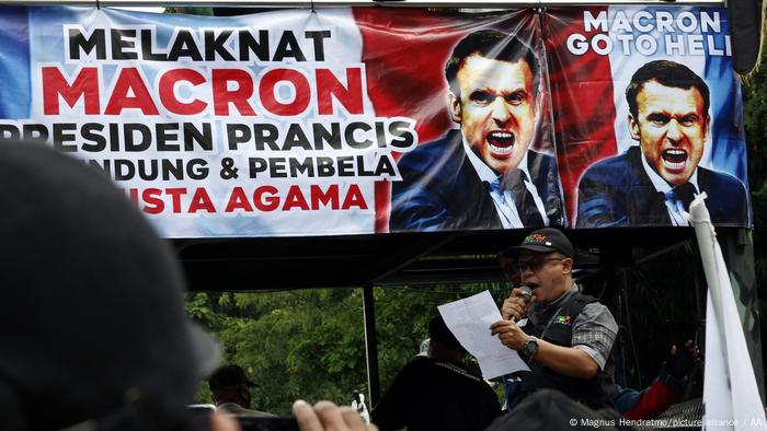 A man in Indonesia stands in front of a banner protesting Macron and speaks into a microphone (Magnus Hendratmo/picture alliance / AA)