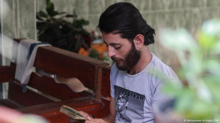 A young man sits, looking downcast as he reads a document.